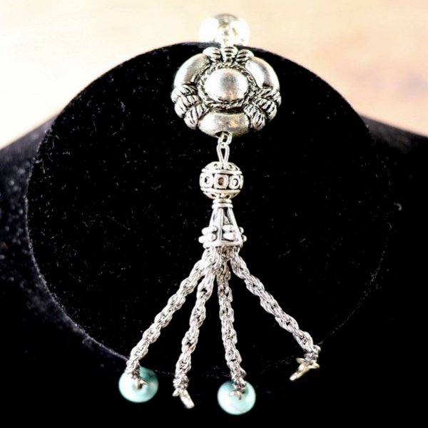 Motiv 2: Runder, flacher Anhänger mit Kettchen an denen türkise Perlen und Blättchen hängen